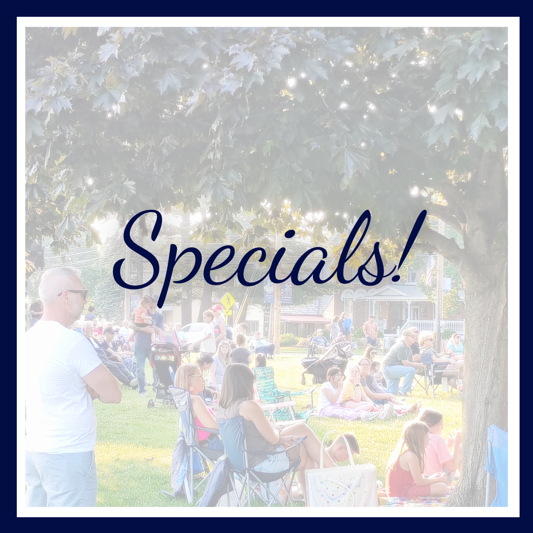 featured "A photo of people gathered outdoors at a community event, sitting on lawn chairs and blankets under a large leafy tree. The scene is framed with a thick navy border, and the word 'Specials!' appears in large cursive text across the center."